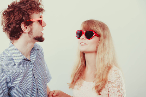 Happy young couple in heart shaped glasses. Smiling friends woman and man in studio. - Foto, afbeelding