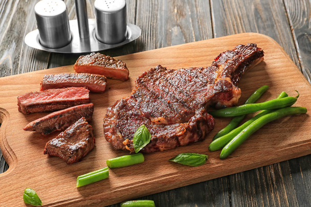 Plateau avec de délicieux steaks grillés et haricots verts sur table en bois
 - Photo, image