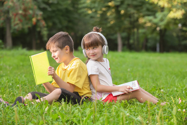 Bambini piccoli e carini che leggono libri e ascoltano musica nel parco durante la giornata estiva
 - Foto, immagini