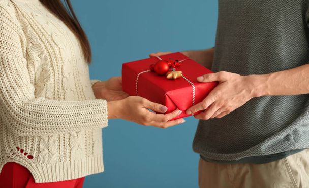 niedliches junges Paar mit Weihnachtsgeschenk auf farbigem Hintergrund - Foto, Bild