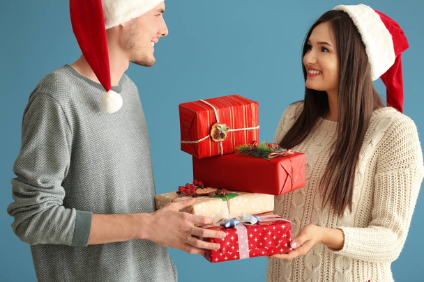 Cute young couple with Christmas gifts on color background - Foto, imagen