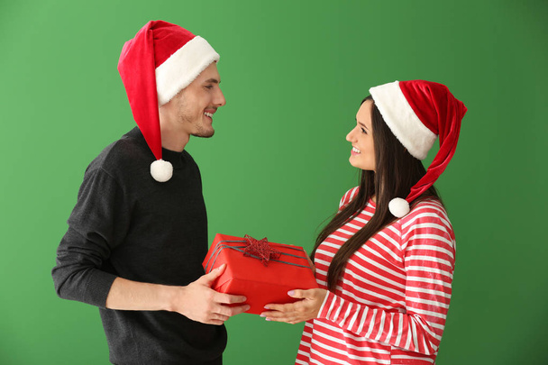 Χαριτωμένο νεαρό ζευγάρι με το δώρο Χριστουγέννων σε χρώμα φόντου - Φωτογραφία, εικόνα