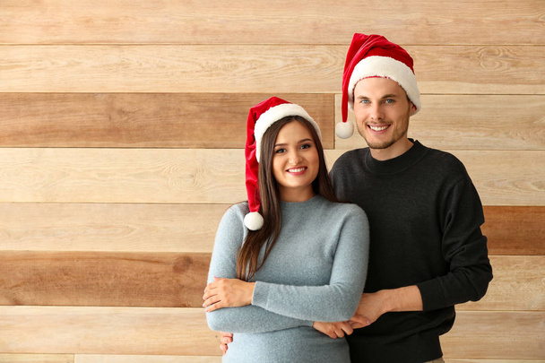 Portrait of cute young couple in Santa hats on wooden background - Zdjęcie, obraz