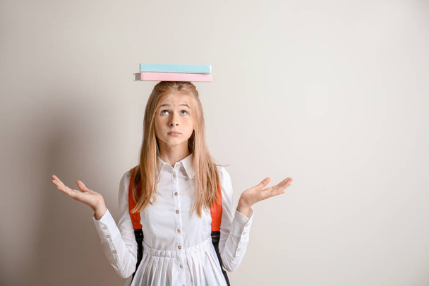 Χαριτωμένο μαθήτρια με βιβλία στο κεφάλι ενάντια σε ανοιχτόχρωμο φόντο - Φωτογραφία, εικόνα