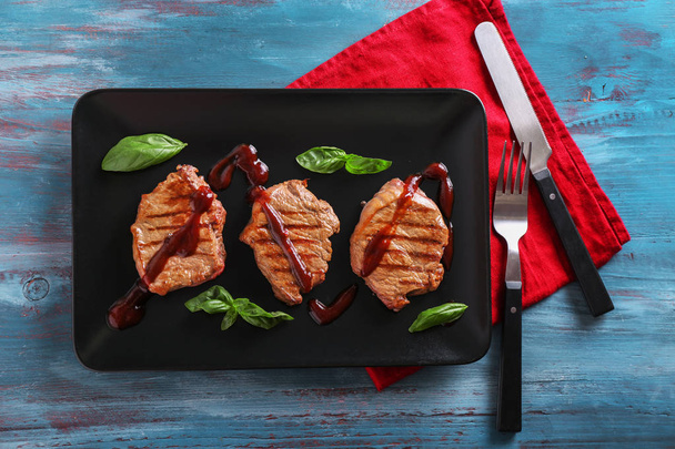 Assiette avec de délicieux steaks grillés et sauce sur table en bois
 - Photo, image