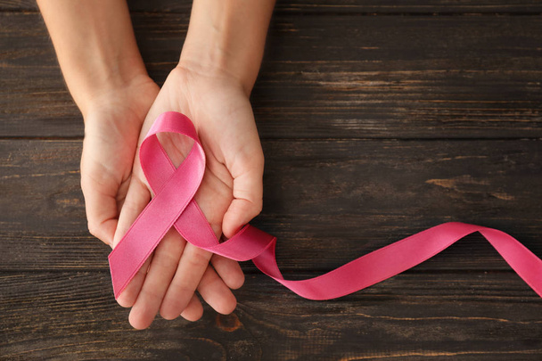 Mujer sosteniendo cinta rosa sobre fondo de madera. Concepto de cáncer de mama
 - Foto, imagen