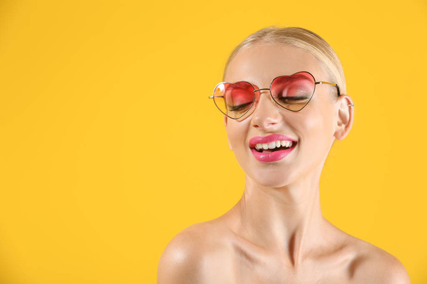 Bella giovane donna con rossetto rosa brillante e occhiali da sole a forma di cuore su sfondo di colore
 - Foto, immagini