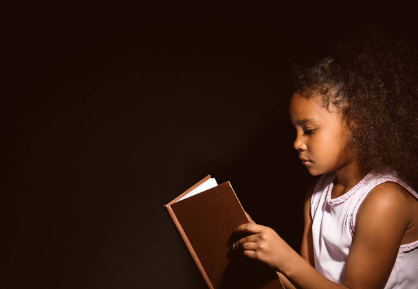 Little African-American girl reading book on dark background - Valokuva, kuva