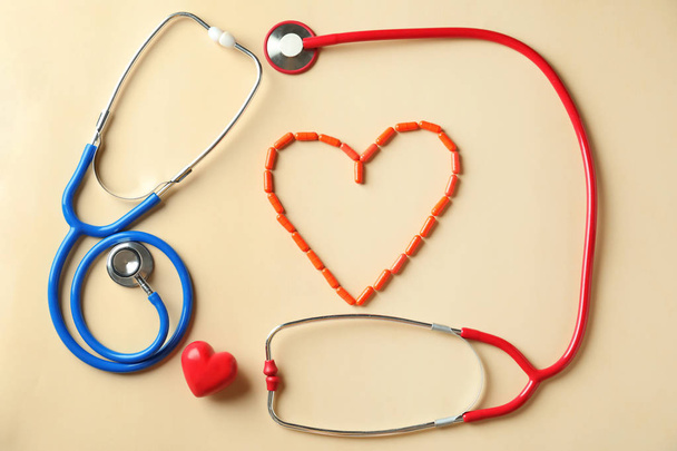 Medical stethoscopes, pills and red heart on light background. Cardiology concept - Photo, Image