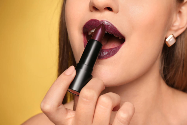Beautiful young woman applying dark lipstick on color background, closeup - Fotoğraf, Görsel