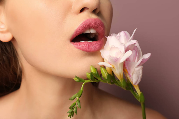 Beautiful young woman with pink lipstick and flower on color background, closeup - 写真・画像
