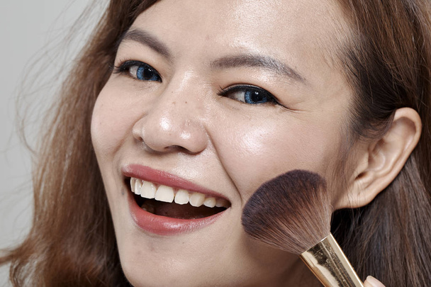 Young beautiful woman applying cosmetic powder brush on face white background. - Photo, Image