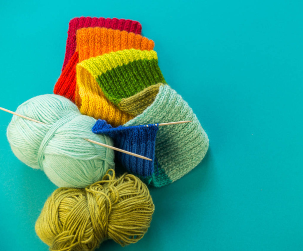 Knitting a rainbow scarf and hat. Basket with balls of wool, knitting needles. Blue background. Favorite work is a hobby. - Фото, зображення