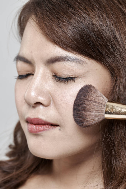 Young beautiful woman applying cosmetic powder brush on face white background. - Fotó, kép