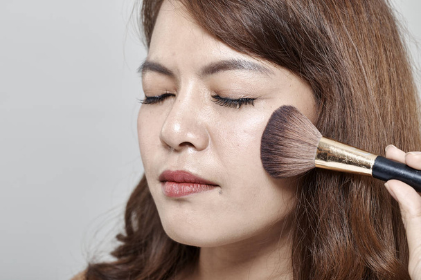 Young beautiful woman applying cosmetic powder brush on face white background. - Foto, Imagen