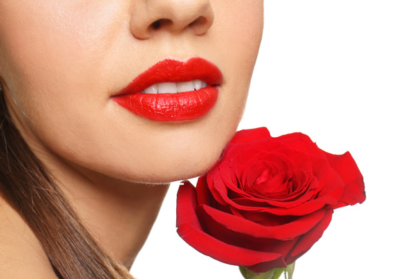 Όμορφη νεαρή γυναίκα με κόκκινο κραγιόν και τριαντάφυλλο σε άσπρο φόντο, κοντινό πλάνο - Φωτογραφία, εικόνα