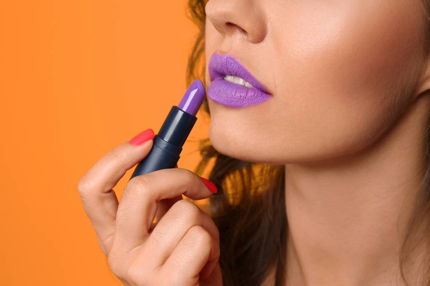 Beautiful young woman applying lilac lipstick on color background, closeup - Photo, Image