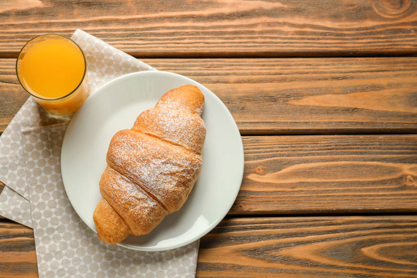 Teller mit leckerem Croissant und einem Glas Orangensaft auf Holztisch - Foto, Bild