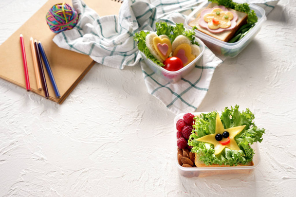 Cajas de almuerzo con bocadillos apetitosos sobre fondo texturizado blanco
 - Foto, Imagen