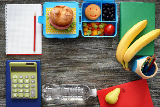 Composición con apetecible comida para escolares y papelería sobre fondo de madera
 - Foto, Imagen