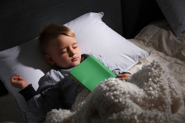 Söpö pieni poika kirjan kanssa nukkuu sängyssä kotona
 - Valokuva, kuva