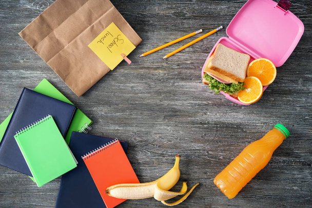 Composition with appetizing food in lunch box and stationery on wooden background - Photo, Image