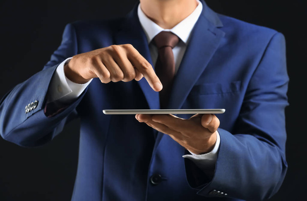 Businessman with tablet PC on dark background, closeup - 写真・画像