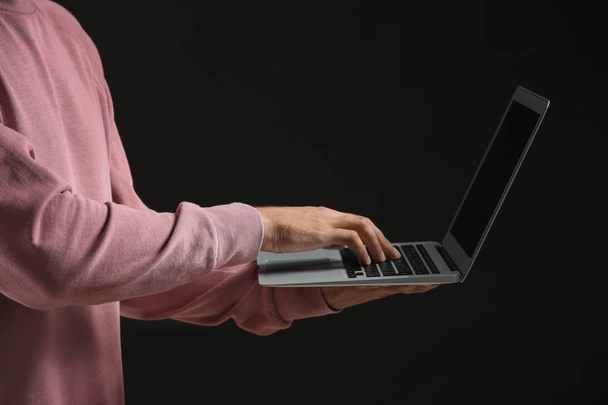Young man with laptop on dark background - Foto, Bild