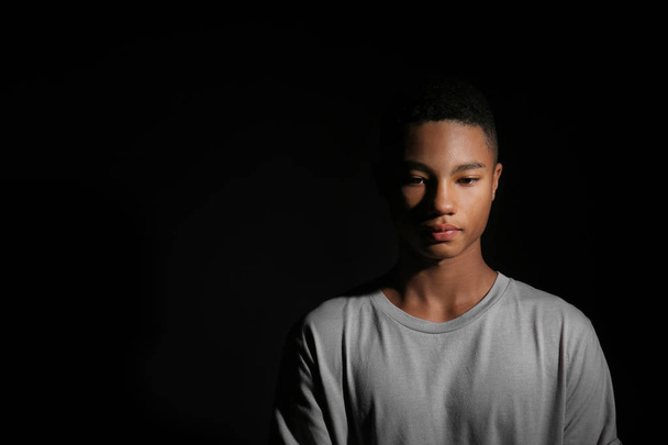Sad African-American teenage boy on dark background - Foto, imagen