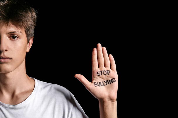 Teenage boy with text STOP BULLYING written on hand against dark background - Photo, Image
