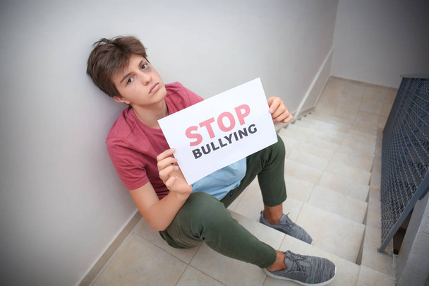 Teenage boy holding sheet of paper with text STOP BULLYING at school - Foto, immagini