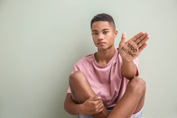 Adolescent afro-américain avec texte STOP BULLYING écrit à portée de main près d'un mur léger
 - Photo, image