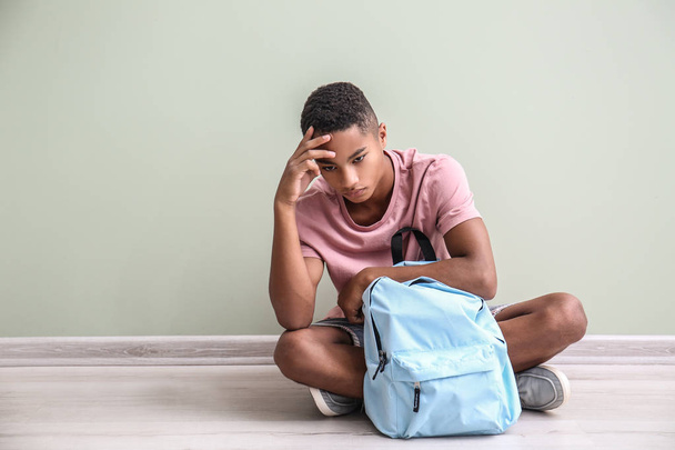 悲しいアフリカ系アメリカ人の 10 代の少年は屋内の床に座って。学校でのいじめ - 写真・画像