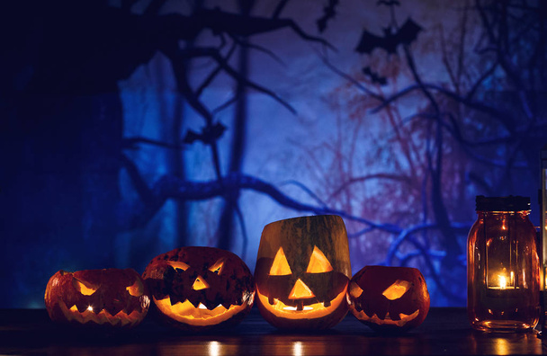 orange pumpkins with scary faces and candles lies on the table in front of dark blue background. Halloween celebration concept - Photo, Image
