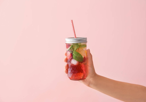 Woman holding jar of fresh strawberry lemonade on color background - Photo, Image