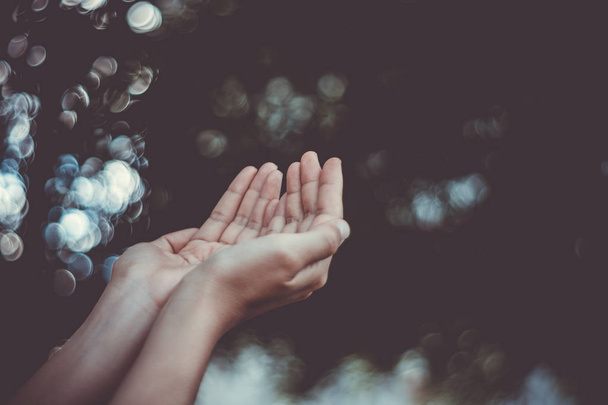 Γυναίκα χέρια θέση μαζί, όπως προσεύχεται μπροστά από τη φύση πράσινο bokeh και μπλε φόντο του ουρανού. - Φωτογραφία, εικόνα