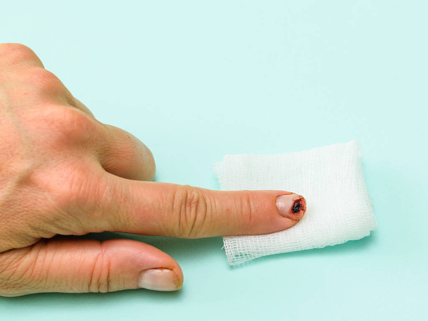 Mano femenina con el dedo dañado en la almohadilla de vendaje sobre fondo azul. Daño a la mano en una situación doméstica
. - Foto, imagen