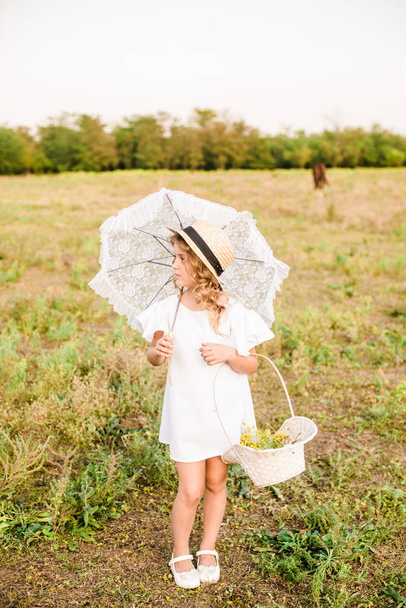 Pěkná malá holčička s světle kudrnaté vlasy v bílých šatech a polem slaměný klobouk s koňmi. Život na venkově v podzim. Koně a lidé - Fotografie, Obrázek