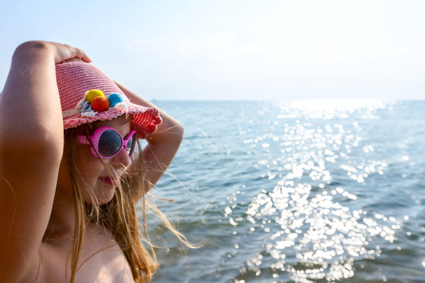 Πορτρέτο της νεαρής γυναίκας, απολαμβάνει το παιδί το καλοκαίρι καπέλο και γυαλιά ηλίου στην ακτή της θάλασσας. - Φωτογραφία, εικόνα