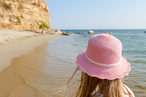 若い女性は、帽子と花のドレスは浅い水、海岸のビーチのキュートな夏子に後ろから見た. - 写真・画像