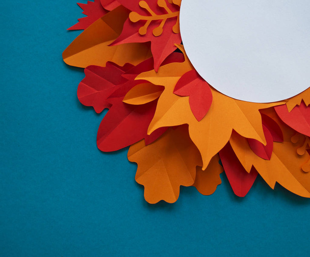 Leaves of paper autumn in a circle. Red, yellow and orange leaves. Place for recording. Blue background. - Foto, Imagen