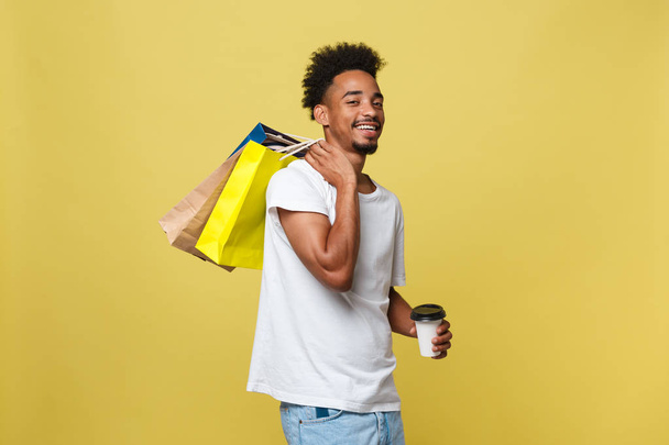 Handsome African American with shopping bag and take away coffee cup. Isolated over yellow gold background. - Фото, зображення