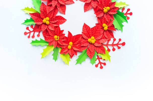 Paper flower poinsettia and leaves of holly. Christmas wreath. White background. Colors are green, red, yellow. - Photo, Image