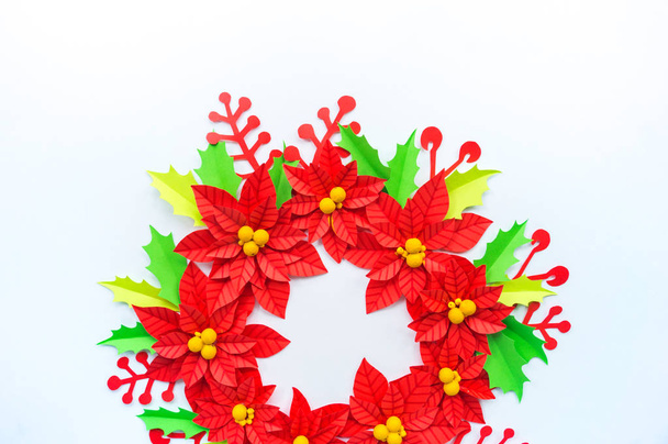 Paper flower poinsettia and leaves of holly. Christmas wreath. White background. Colors are green, red, yellow. - Fotografie, Obrázek