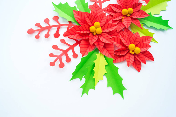Paper flower poinsettia and leaves of holly. Christmas wreath. White background. Colors are green, red, yellow. - Photo, image