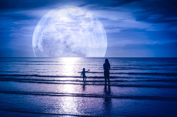Σούπερ Σελήνη. Πολύχρωμο ουρανό με φωτεινά πλήρες φεγγάρι πάνω από το θαλασσινό τοπίο. Σιλουέτα της μητέρας με το παιδί που παίζει στην θάλασσα. Σε υπαίθρια gloaming. Το φεγγάρι που λαμβάνονται με την κάμερα μου. - Φωτογραφία, εικόνα