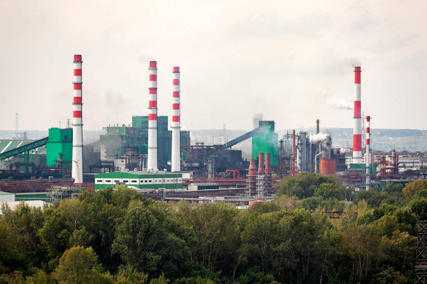 die Landschaft einer riesigen Industriestadt mit Fabriken und hohen Kränen, aus denen riesige Rauchschwaden quellen. Umweltverschmutzung durch Pflanzen und Industrien - Foto, Bild