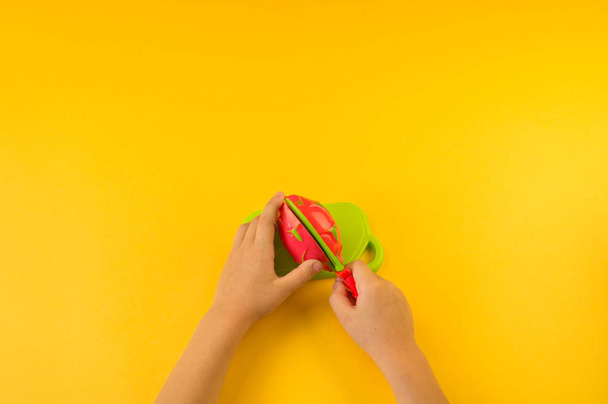 A child cuts a plastic fruit on a board. Children's hands. Playing the cook. yellow background. - Foto, imagen