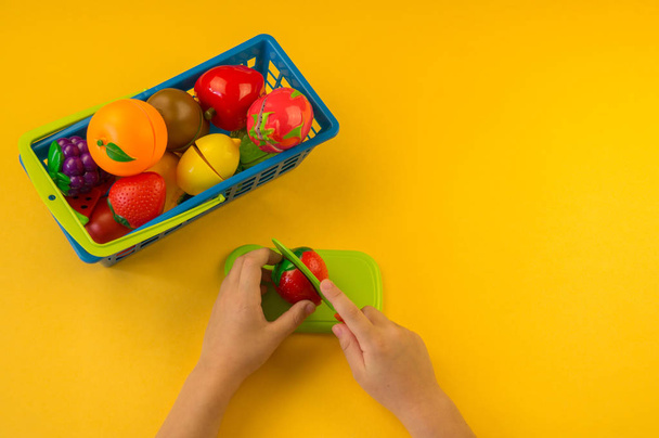 A child cuts a plastic fruit on a board. Children's hands. Playing the cook. yellow background. - Fotoğraf, Görsel