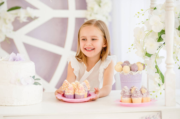 Little girl holding a pink plate with sweet cakes in the candy bar - Fotó, kép